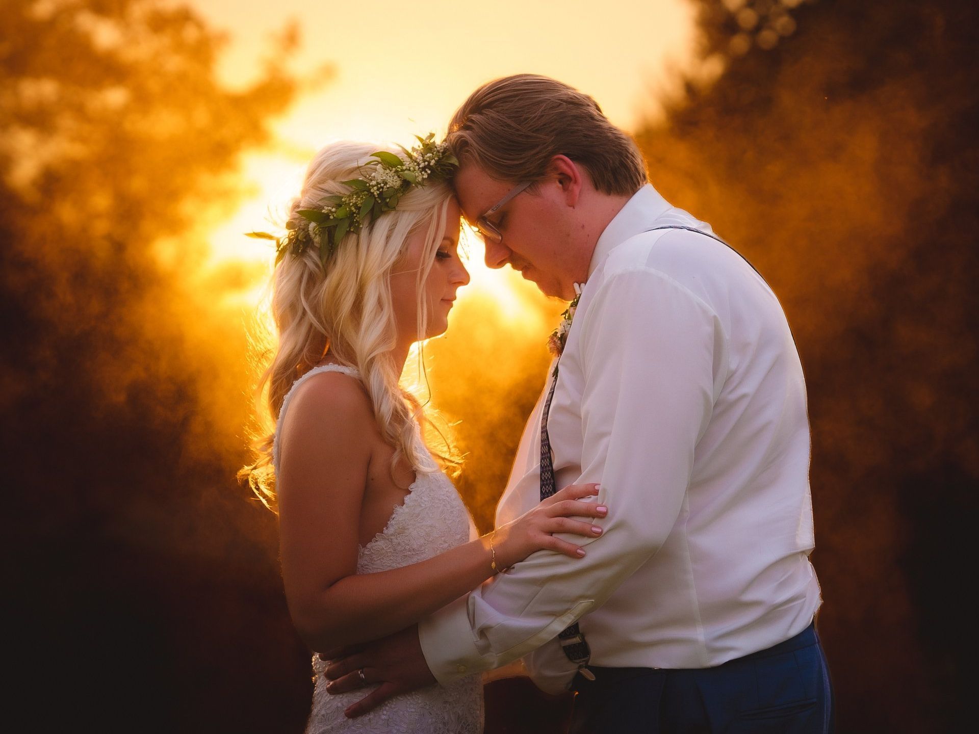 A bride and groom are looking into each other 's eyes at sunset.
