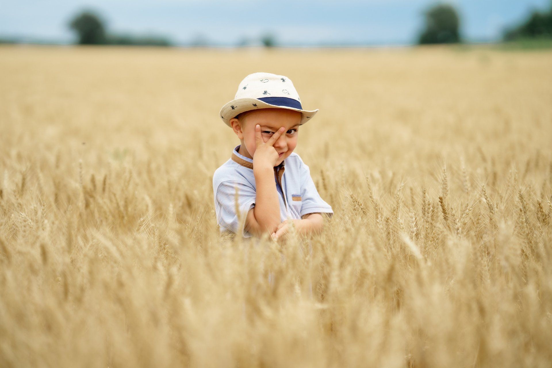 A little boy in a hat is sitting in a field of wheat.