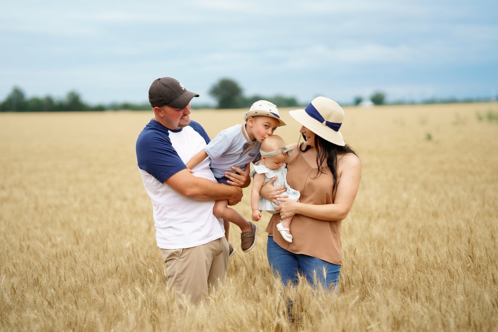 A family is standing in a wheat field holding their children.