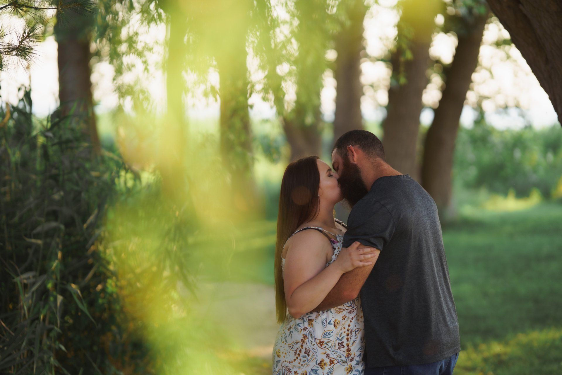 A man and a woman are kissing under a tree in a park.