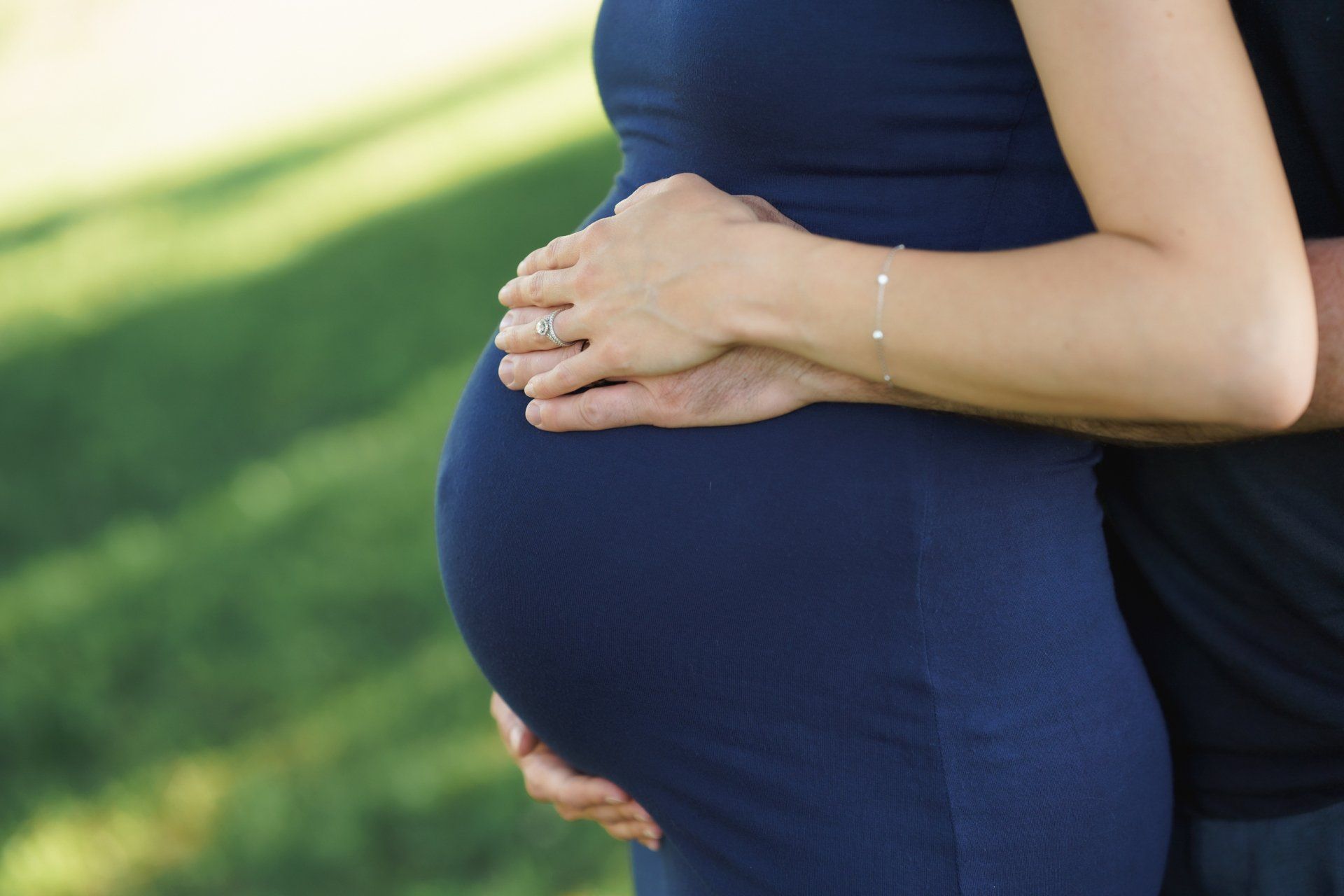 A pregnant woman in a blue dress is being hugged by a man.
