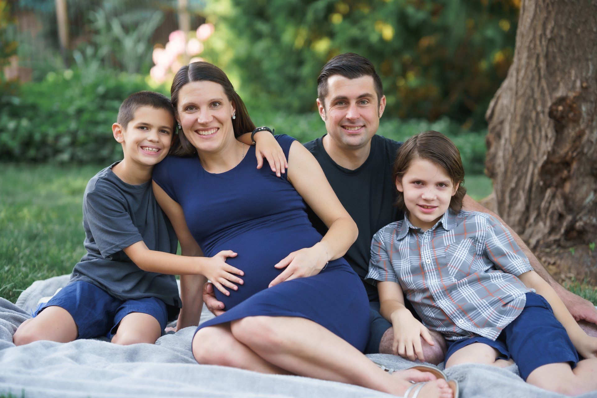 A pregnant woman is sitting on a blanket with her family.