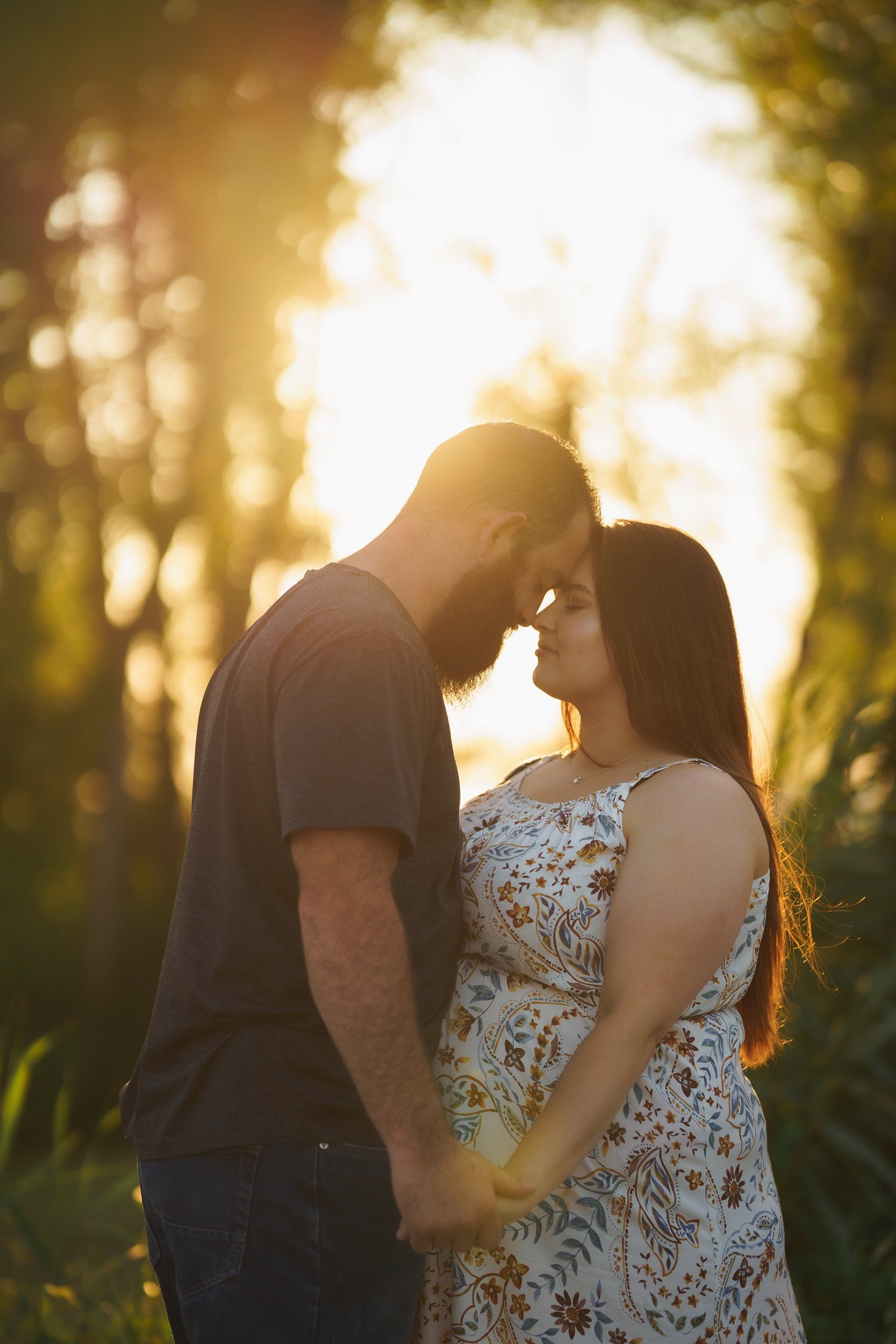 A man and a pregnant woman are kissing in a field.
