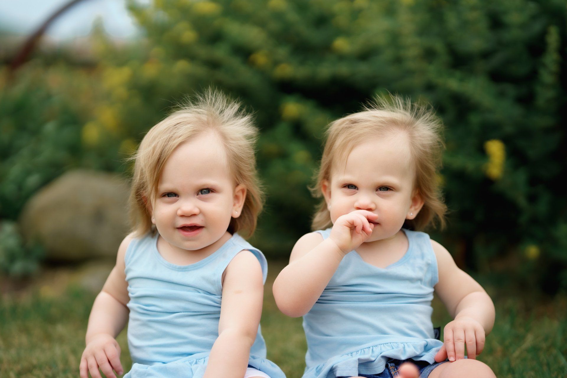 Two little girls are sitting next to each other in the grass.