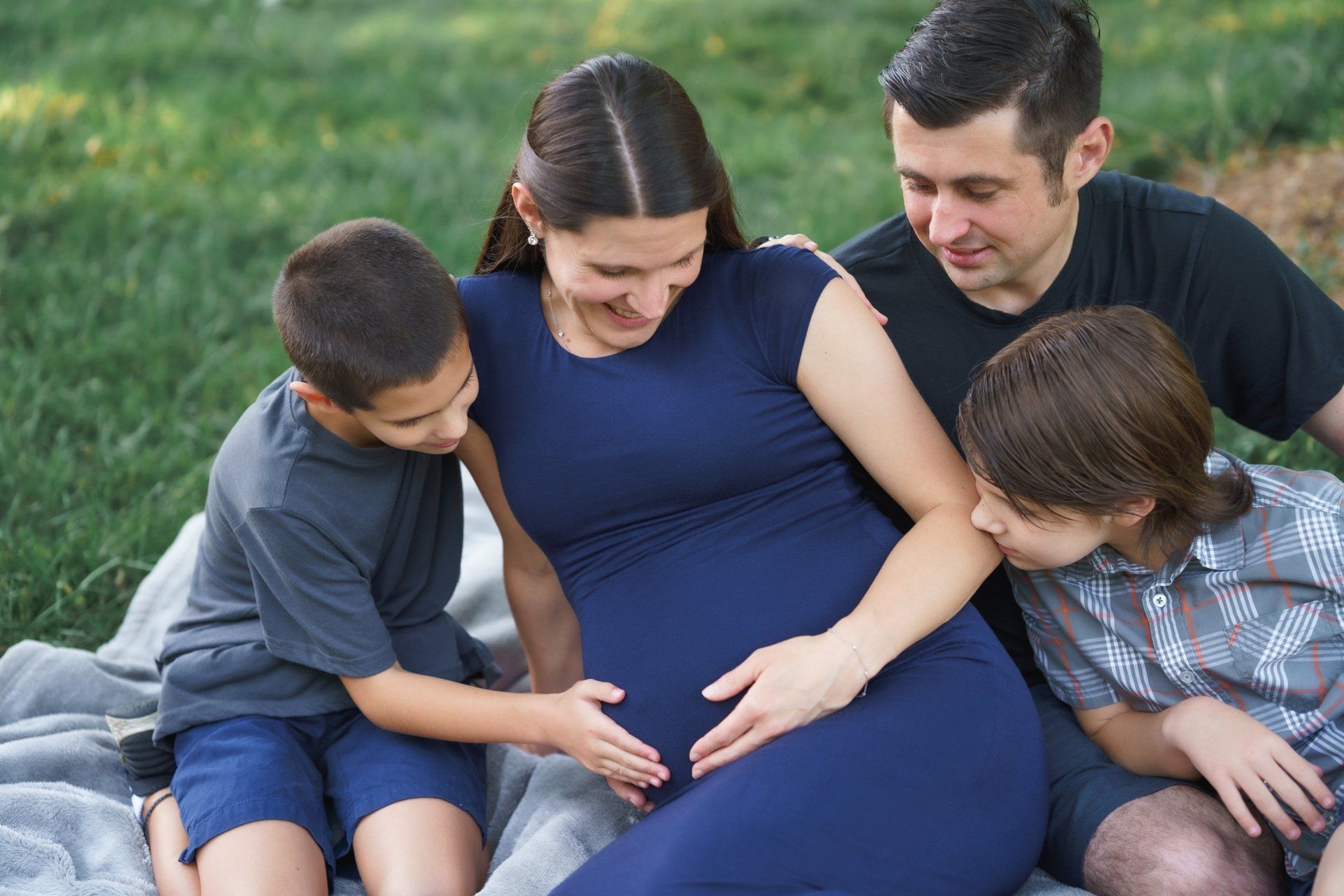 A pregnant woman is sitting on a blanket with her family.