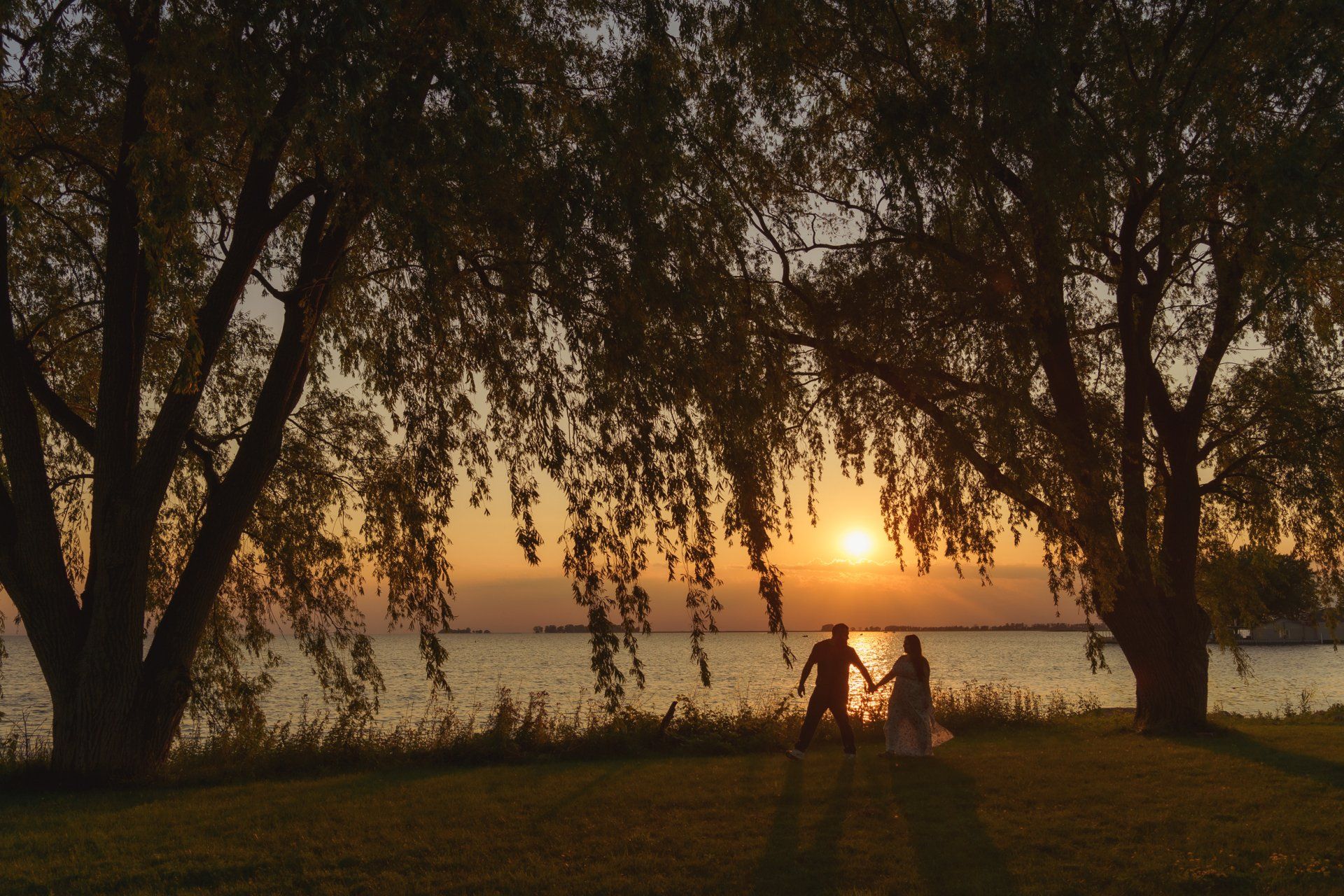 A man and a woman are holding hands in front of a lake at sunset.