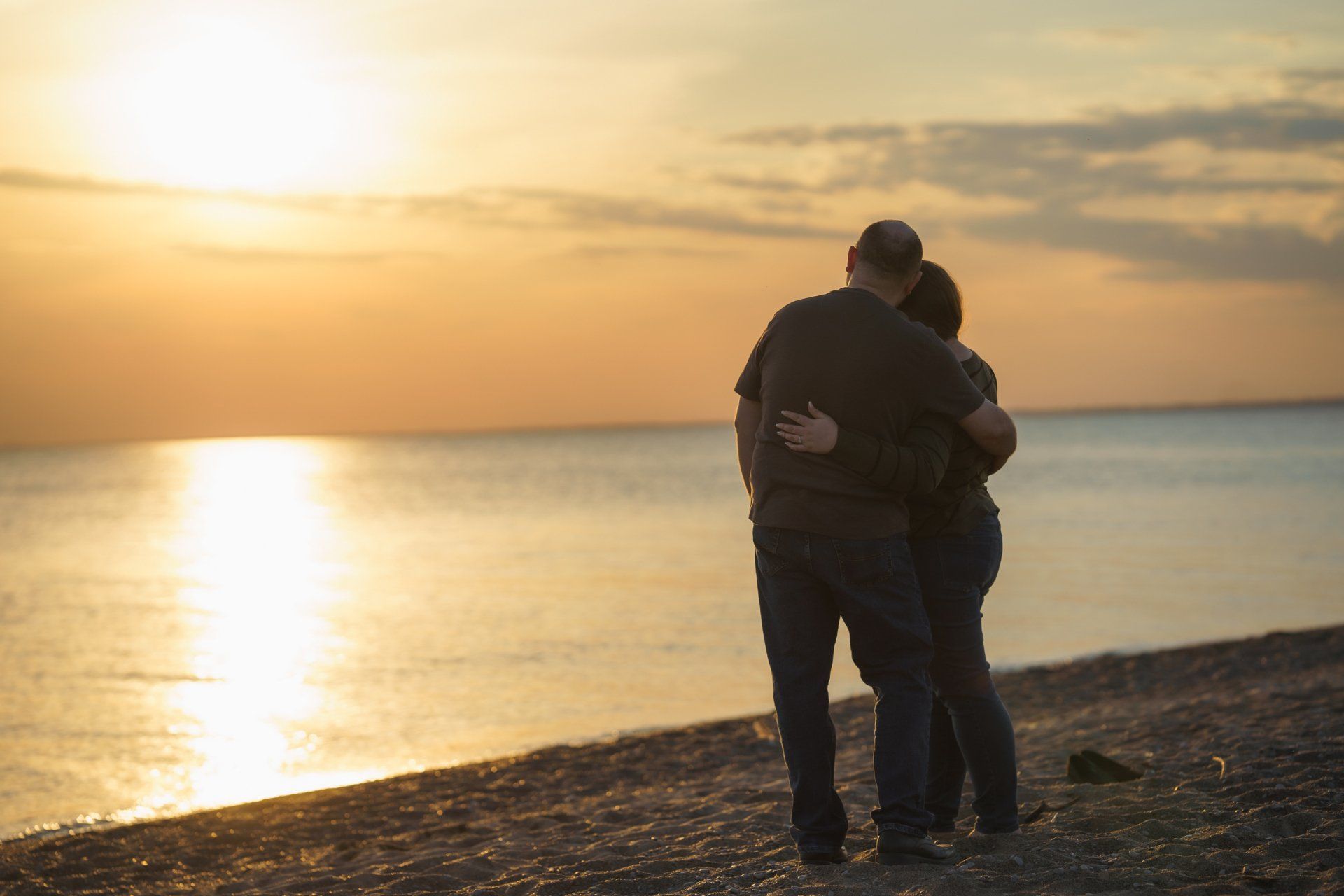 A man and a woman are hugging on the beach at sunset.