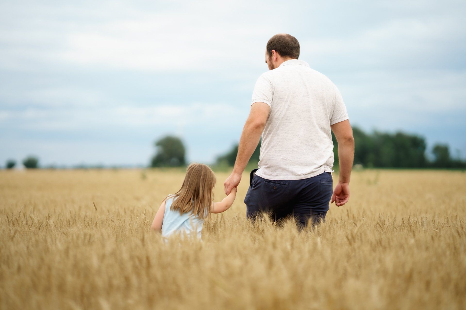 A man and a little girl are walking through a field of wheat holding hands.