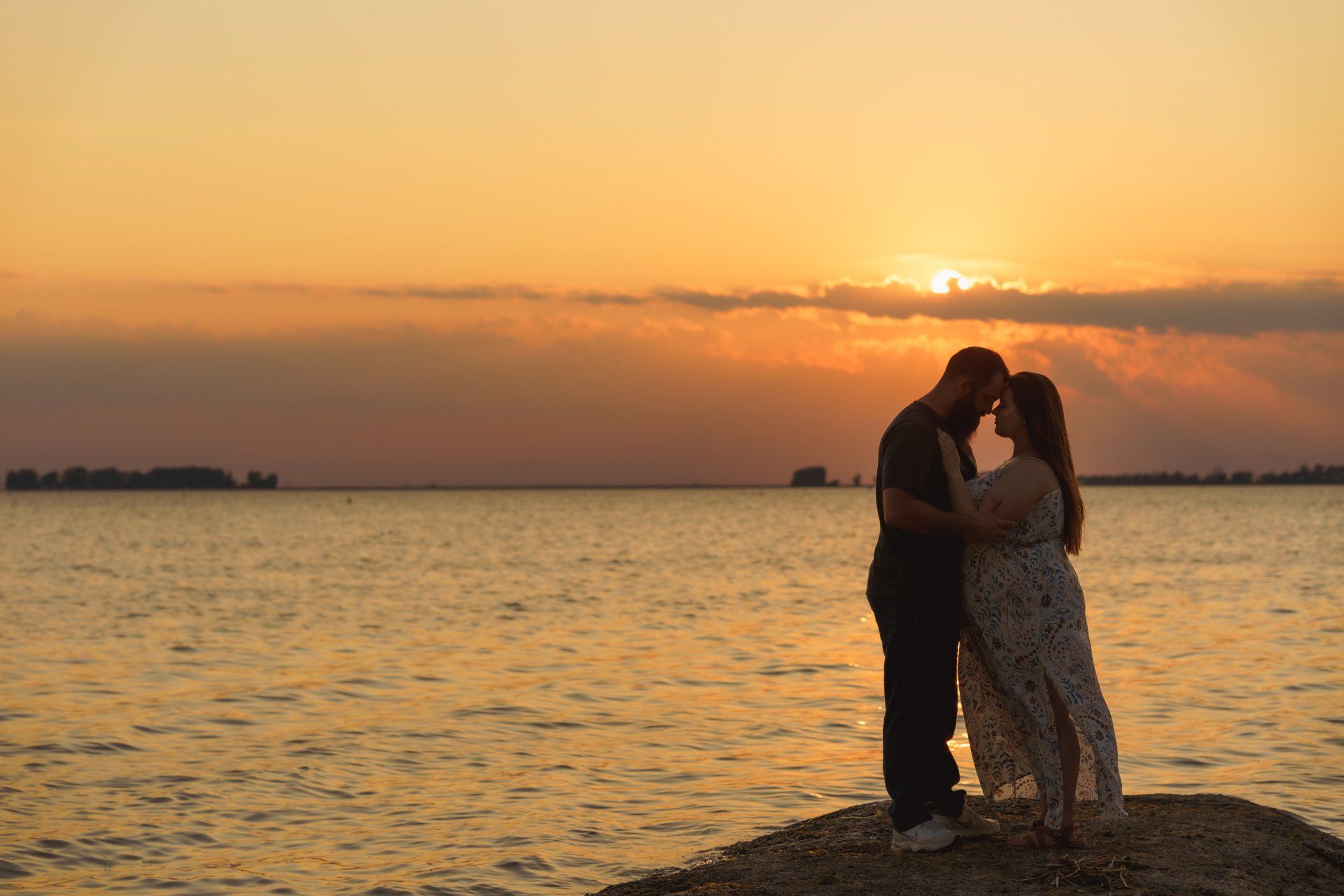 A man and a woman are kissing on the beach at sunset.