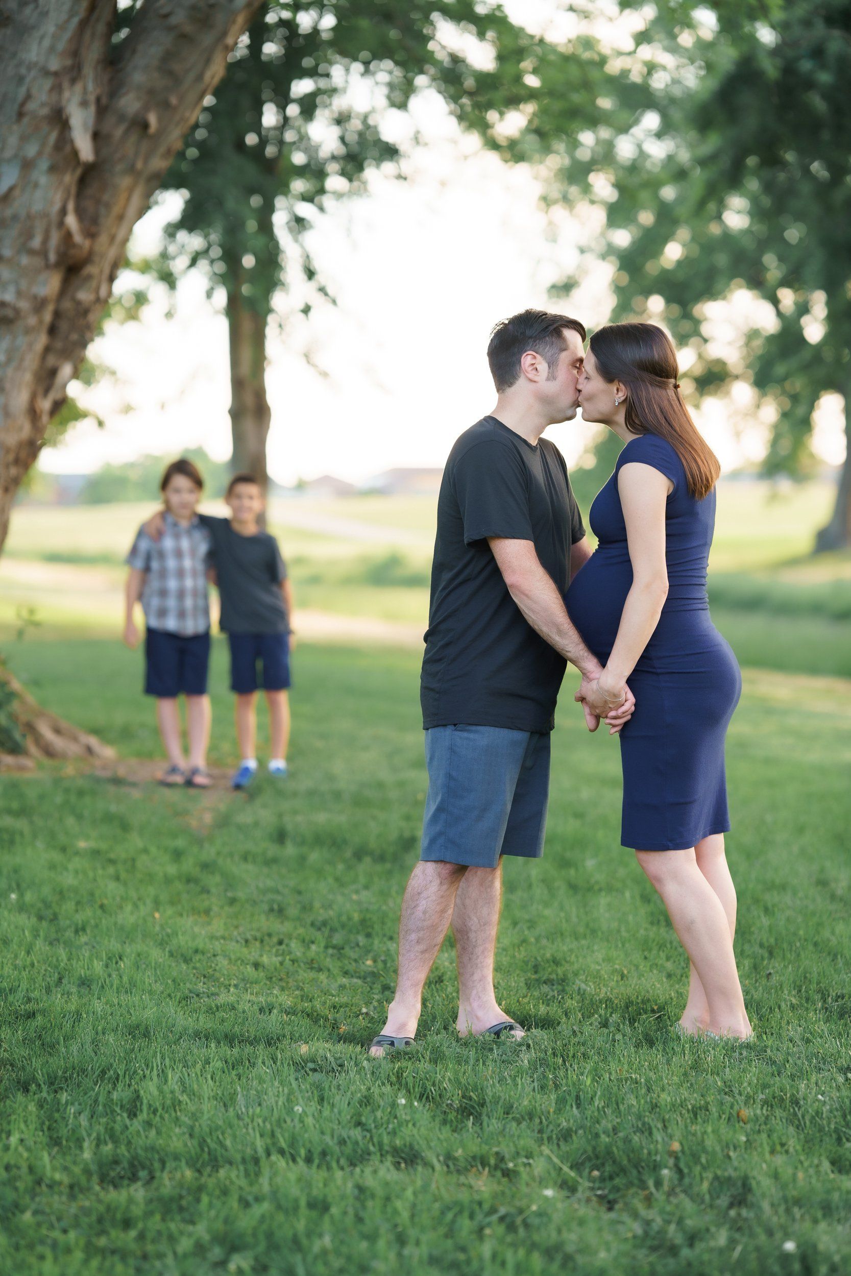 A man and a pregnant woman are kissing in a park.