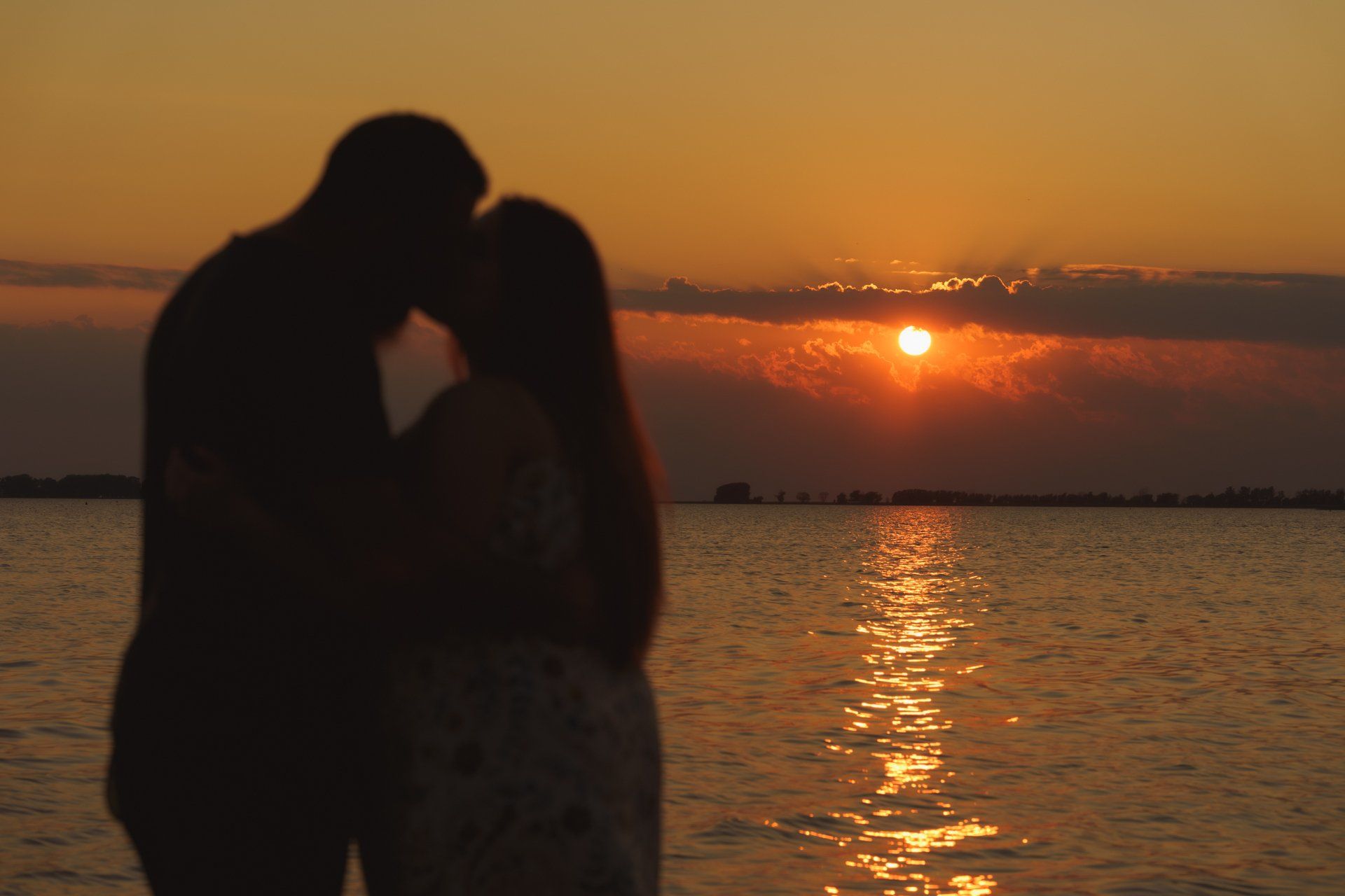 A man and a woman are kissing on the beach at sunset.