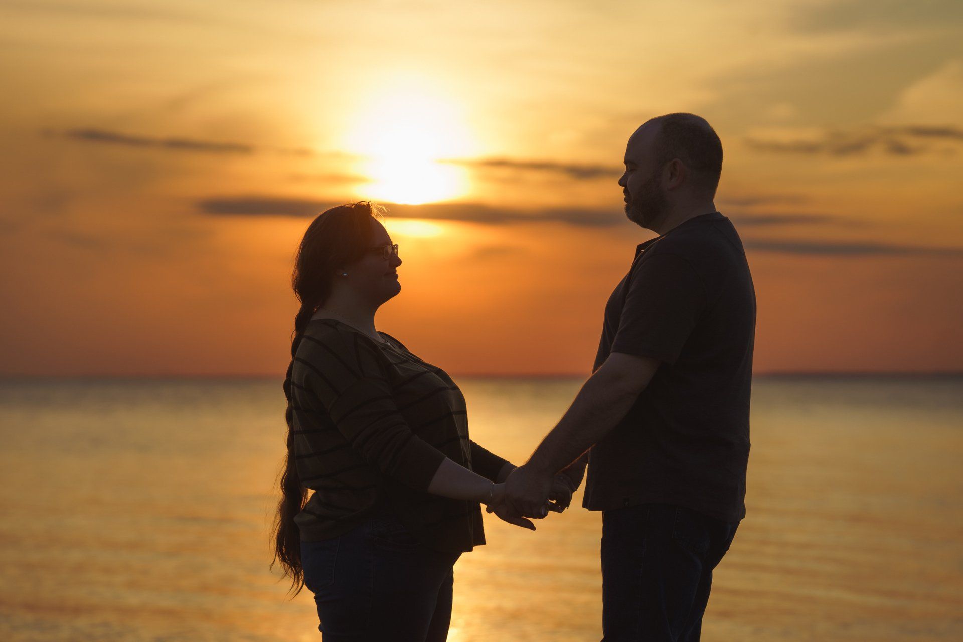 A man and a woman are holding hands on the beach at sunset.