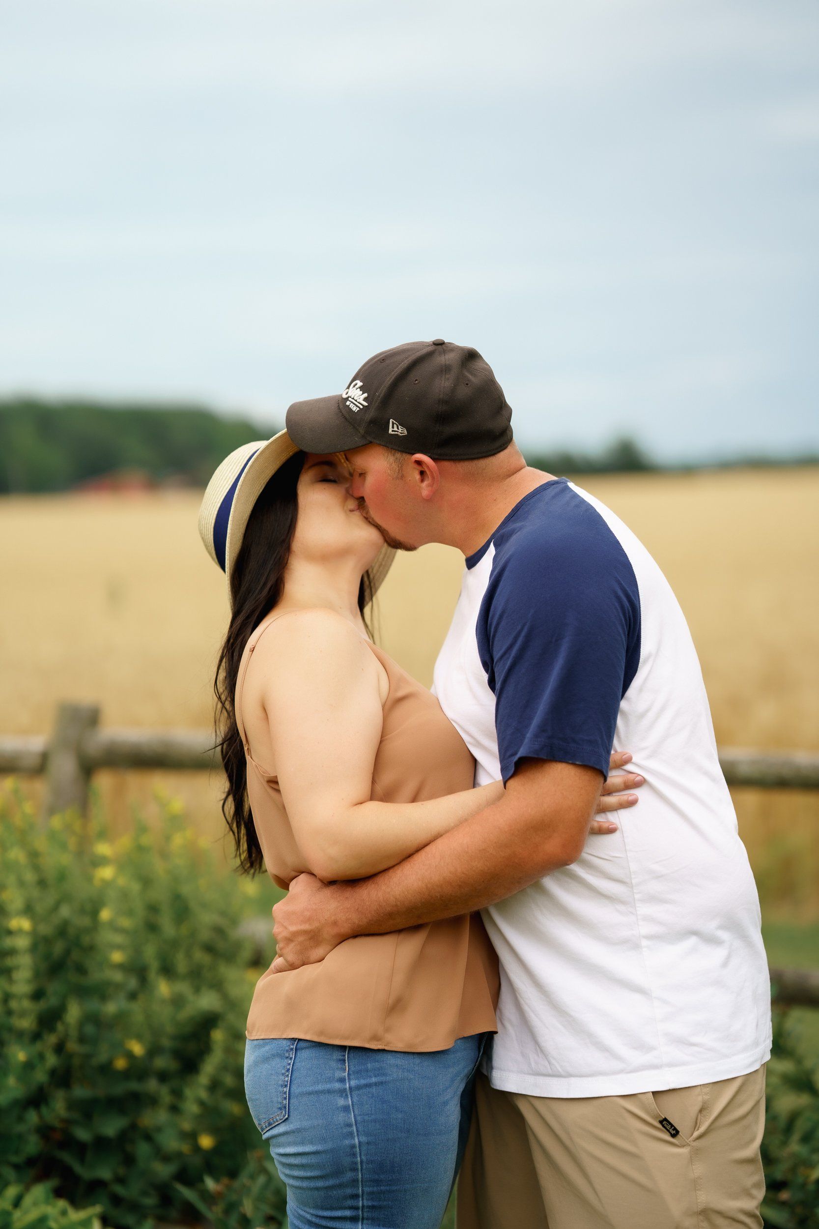 A man and a woman are kissing in front of a field.