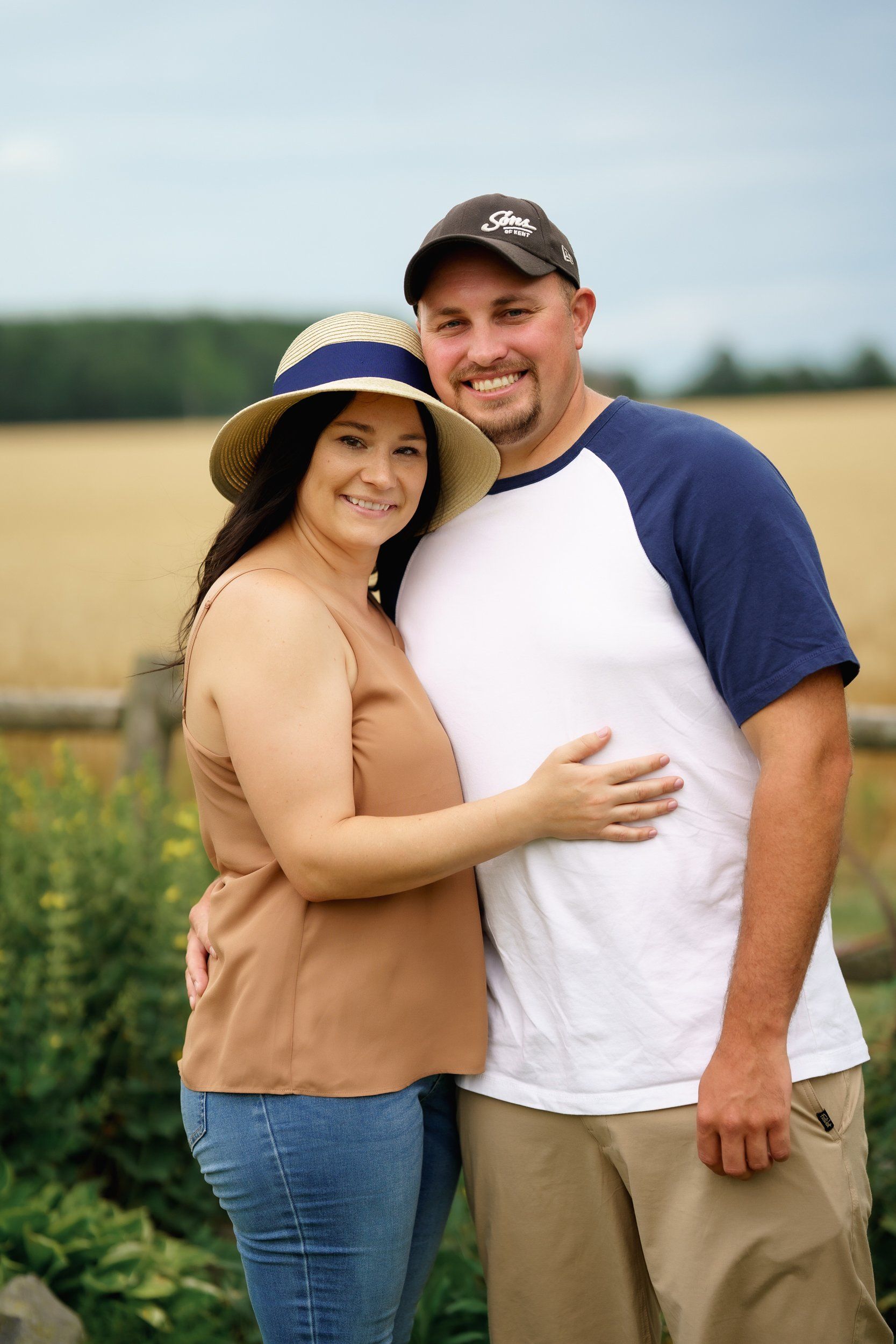 A man and a woman are posing for a picture in front of a field.