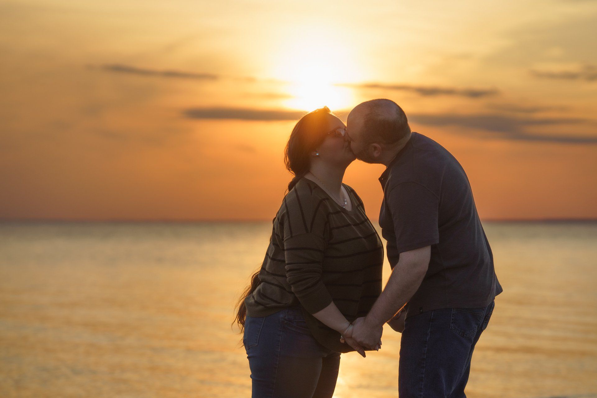 A man and a woman are kissing on the beach at sunset.