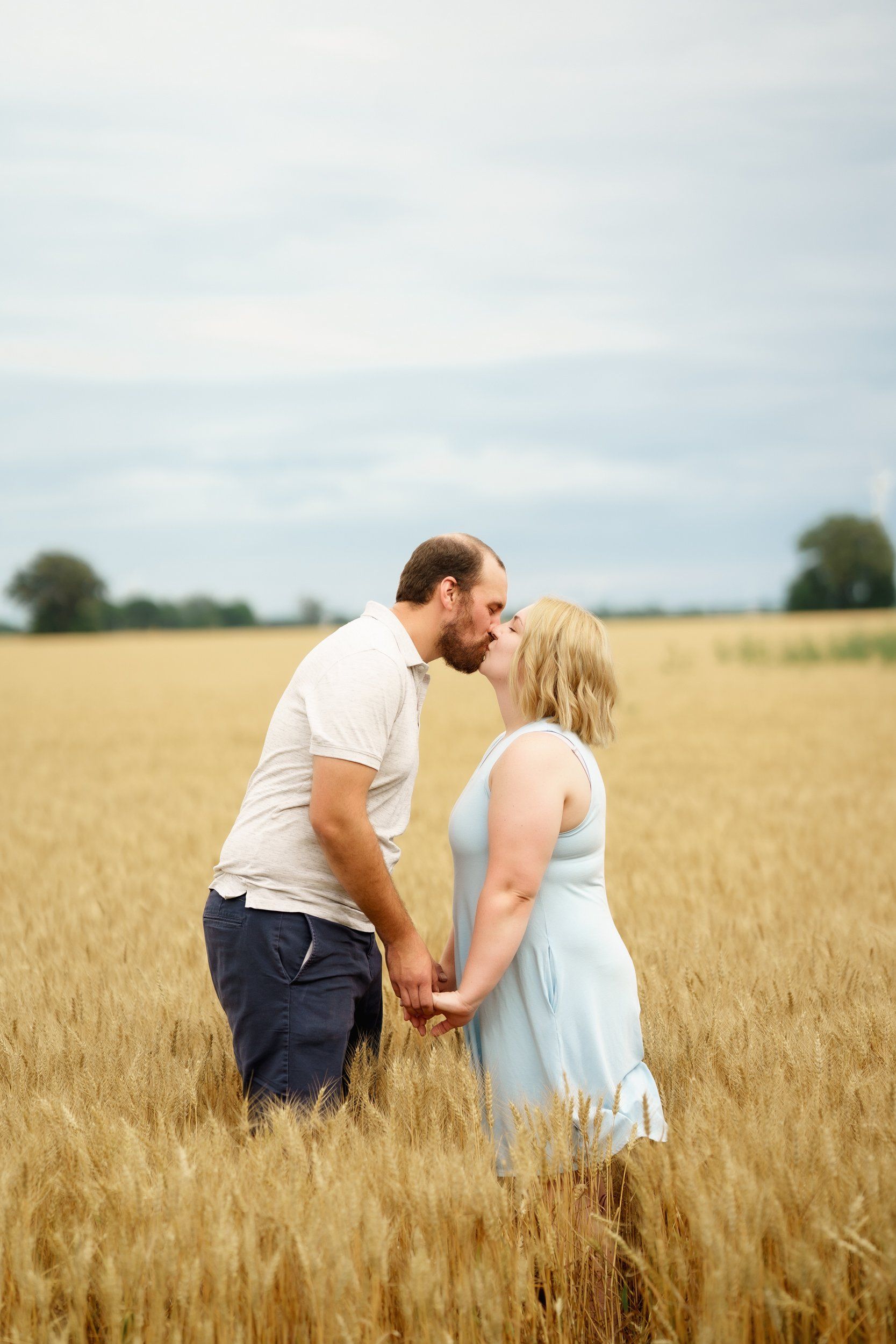 A man and a woman are kissing in a field of wheat.