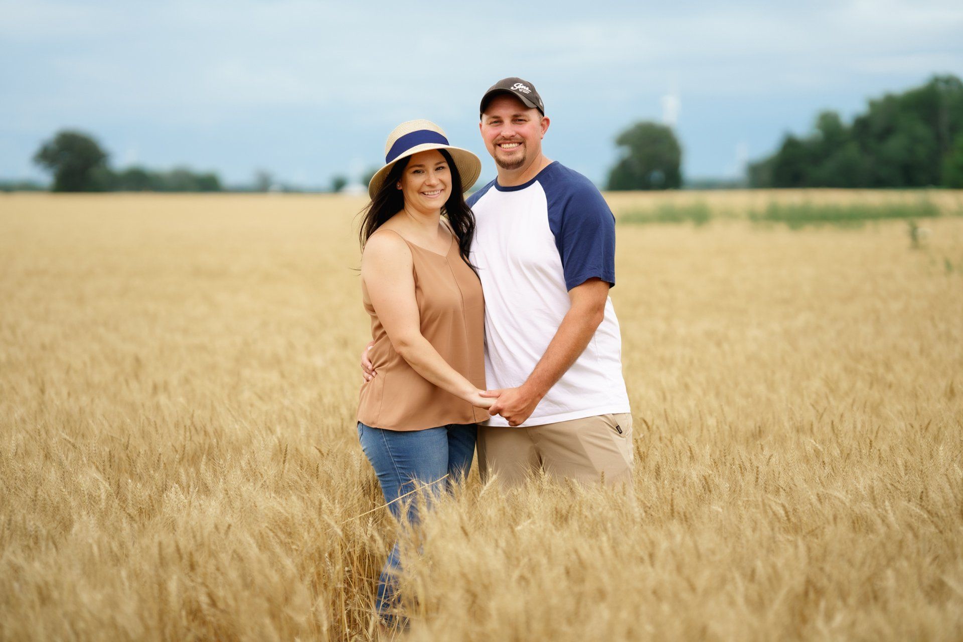 A man and a woman are standing in a wheat field holding hands.