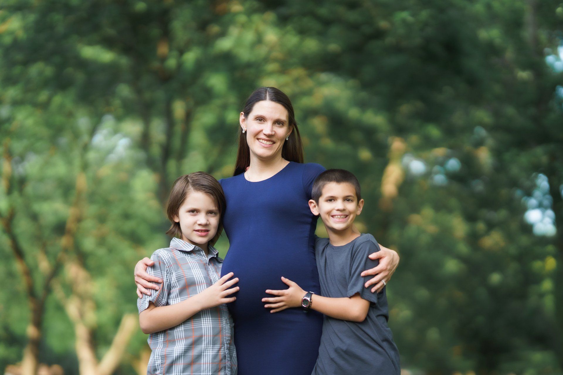 A pregnant woman is standing next to two boys in a park.