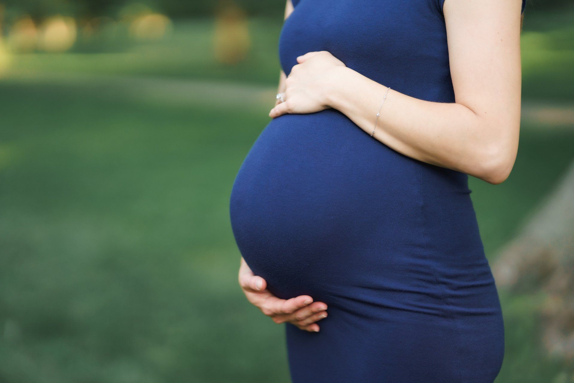 A pregnant woman in a blue dress is holding her belly.