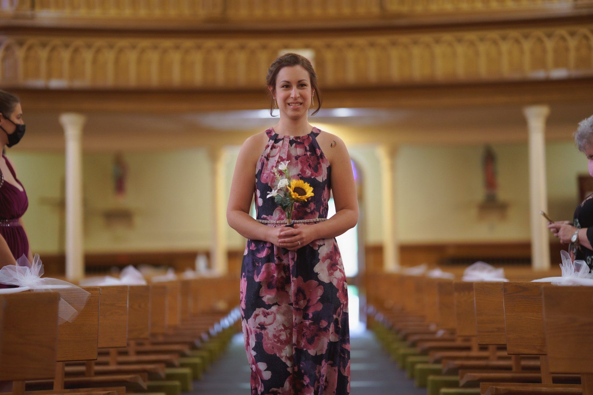 A woman in a floral dress is holding a bouquet of flowers in a church.