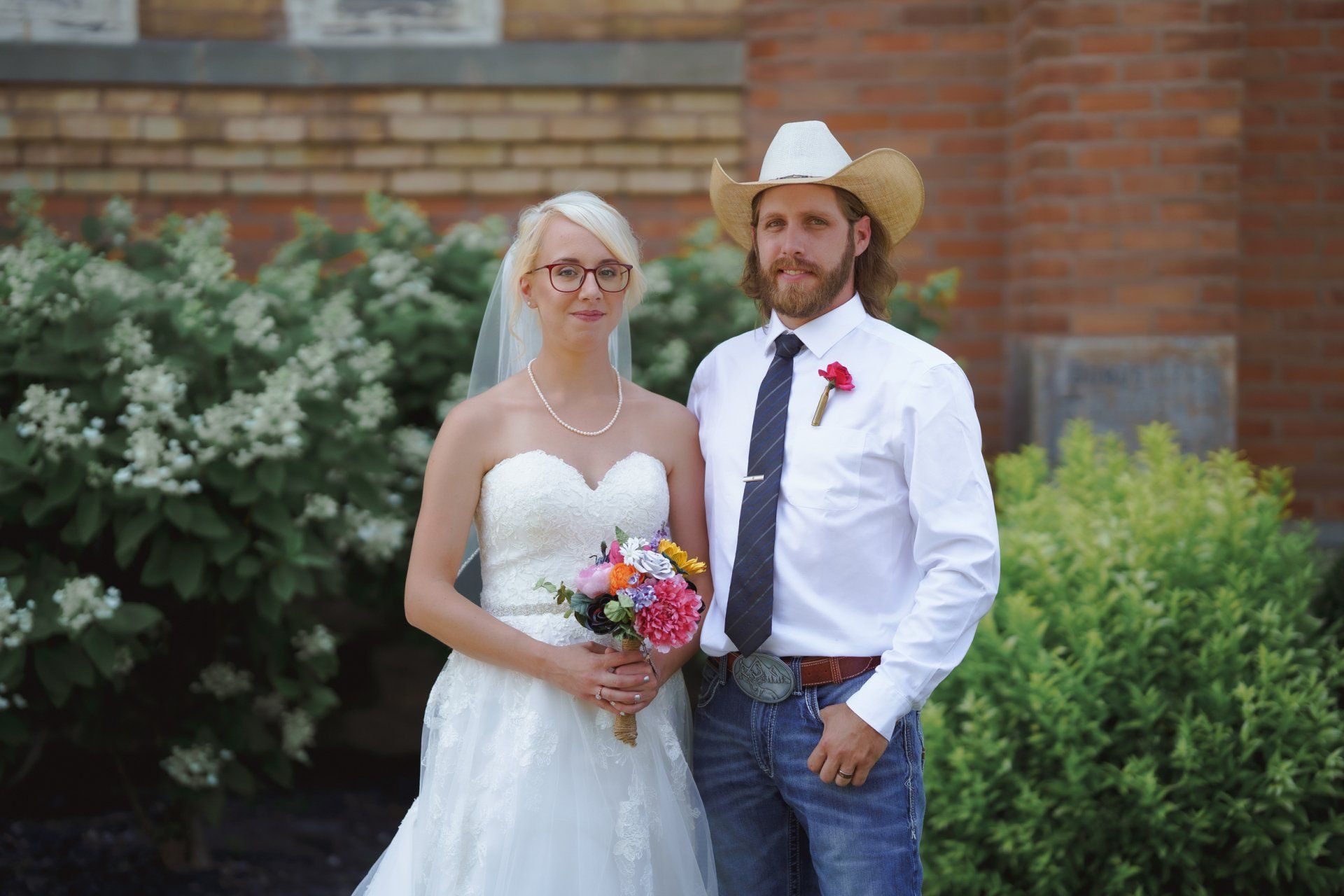 A bride and groom are posing for a picture in front of a brick building.