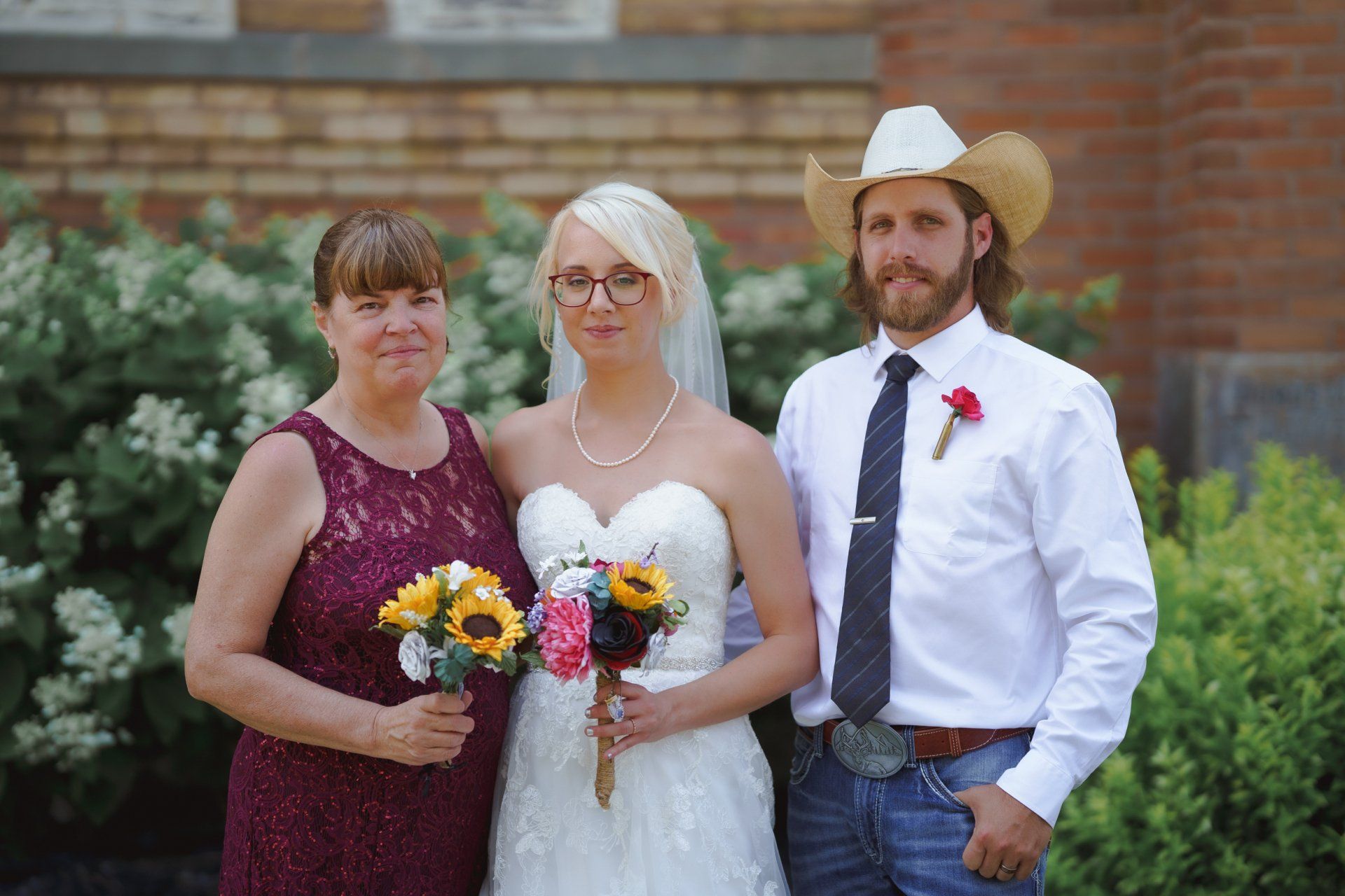 A bride and groom are posing for a picture with their mother and a man in a cowboy hat.