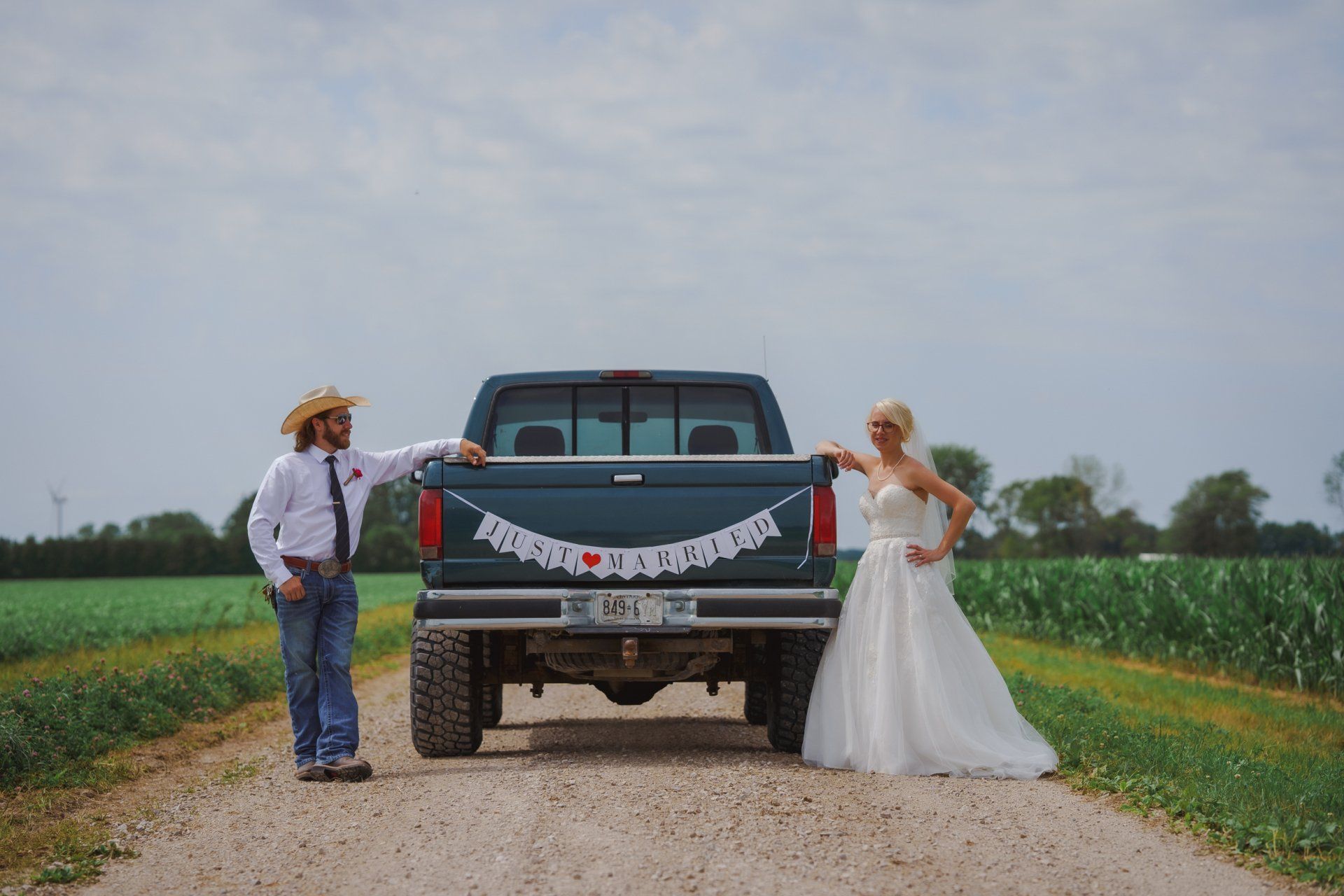 A bride and groom are standing next to a truck on a dirt road.