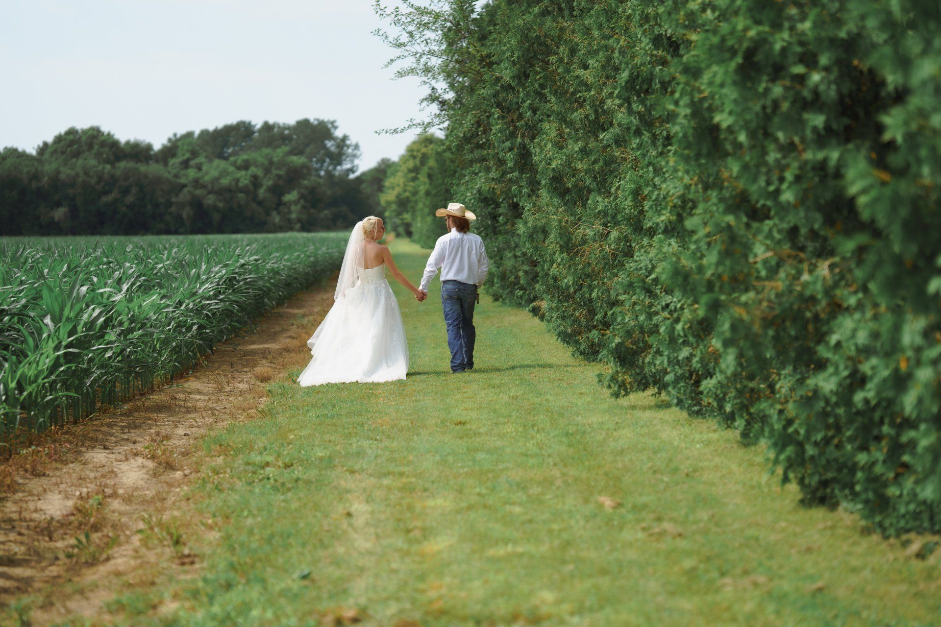 A bride and groom are walking down a path holding hands.