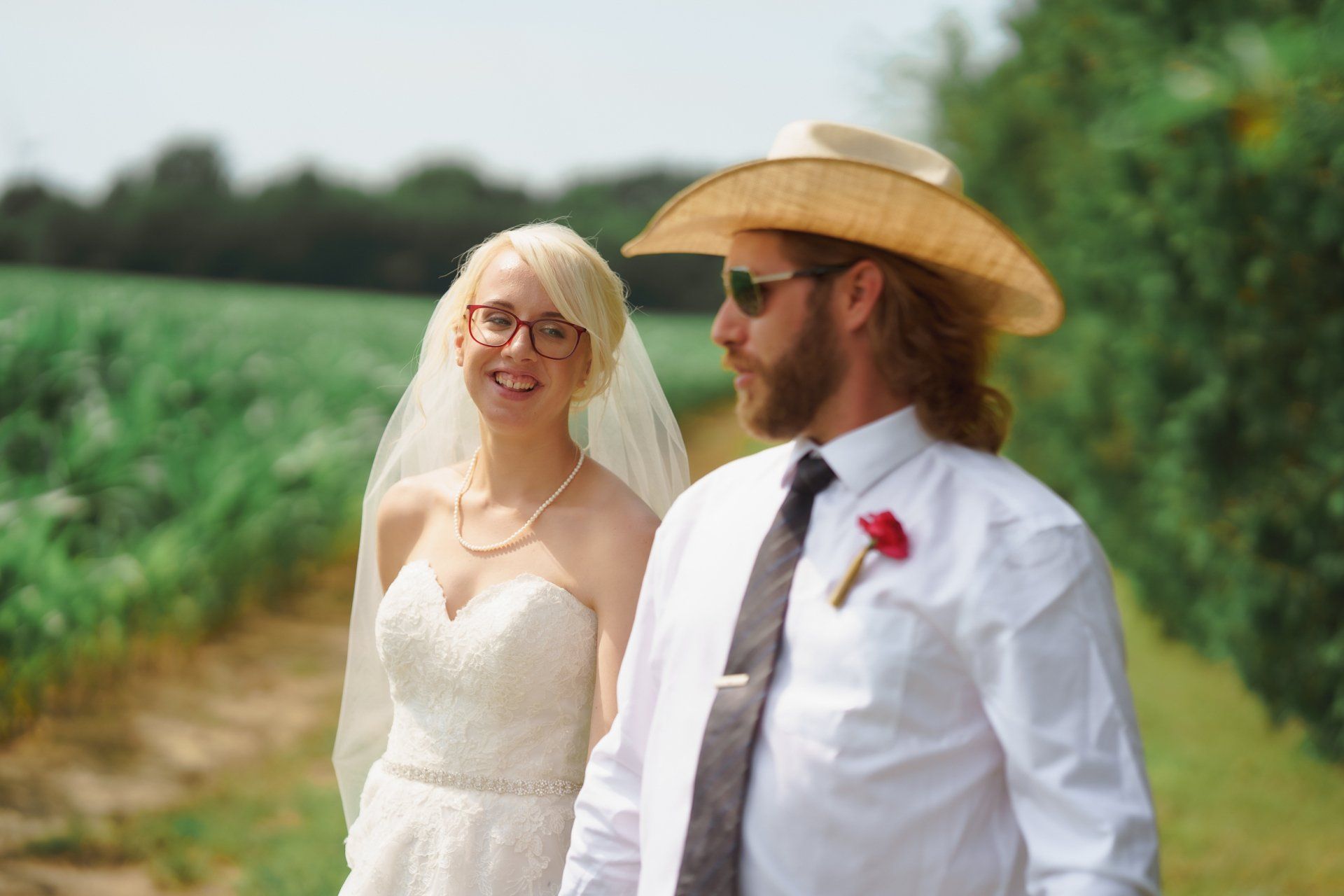 A bride and groom are walking down a path in a field.
