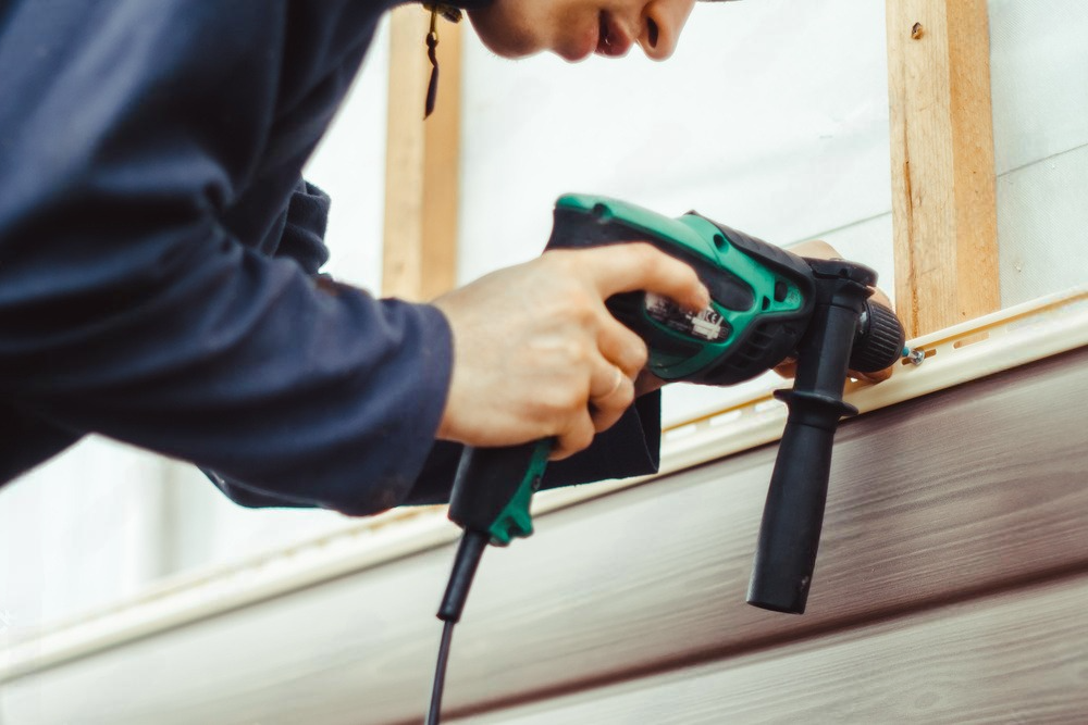 a man is using a hammer drill to install siding on a wall .