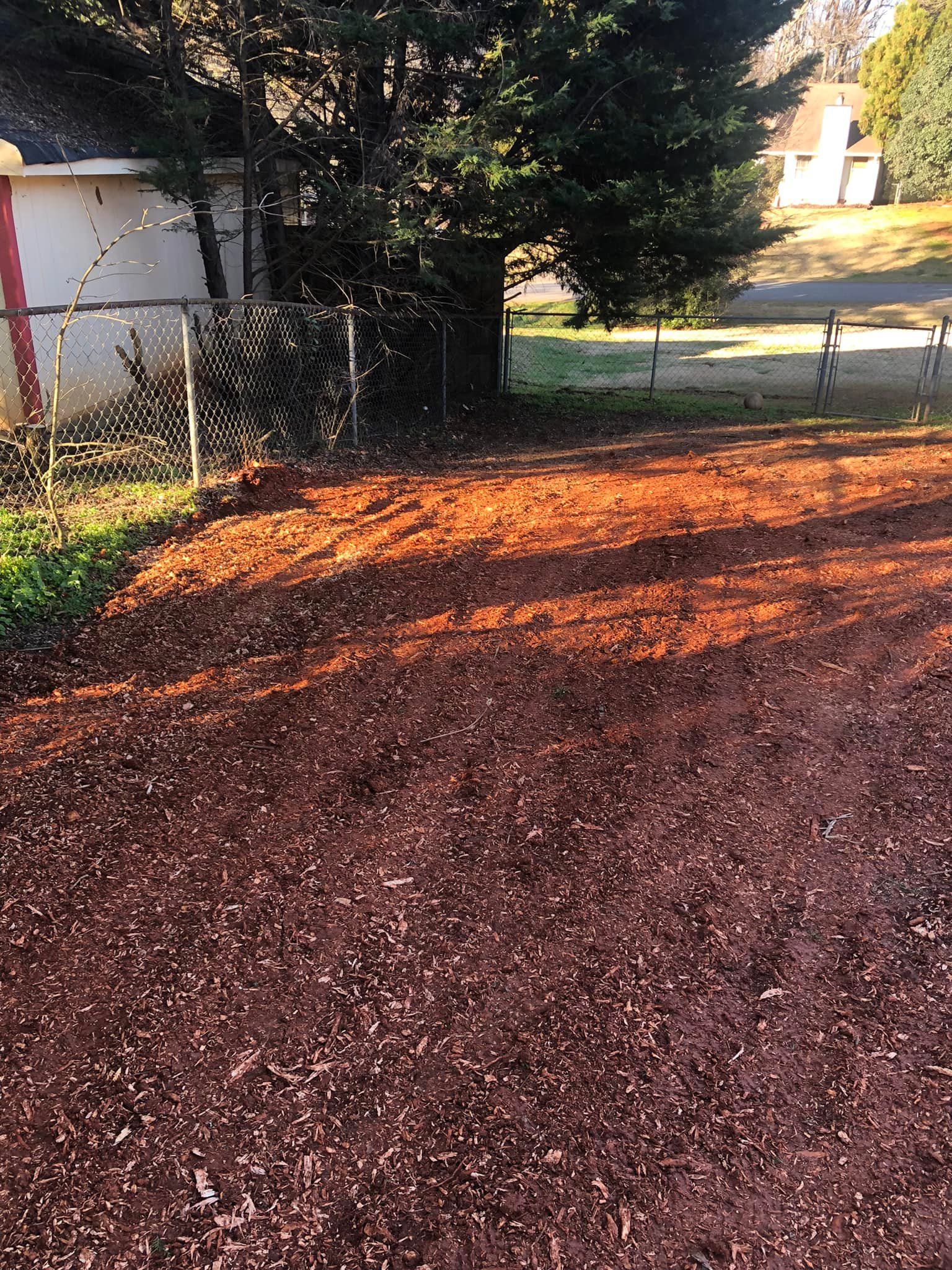 A dirt yard with a fence and a house in the background.