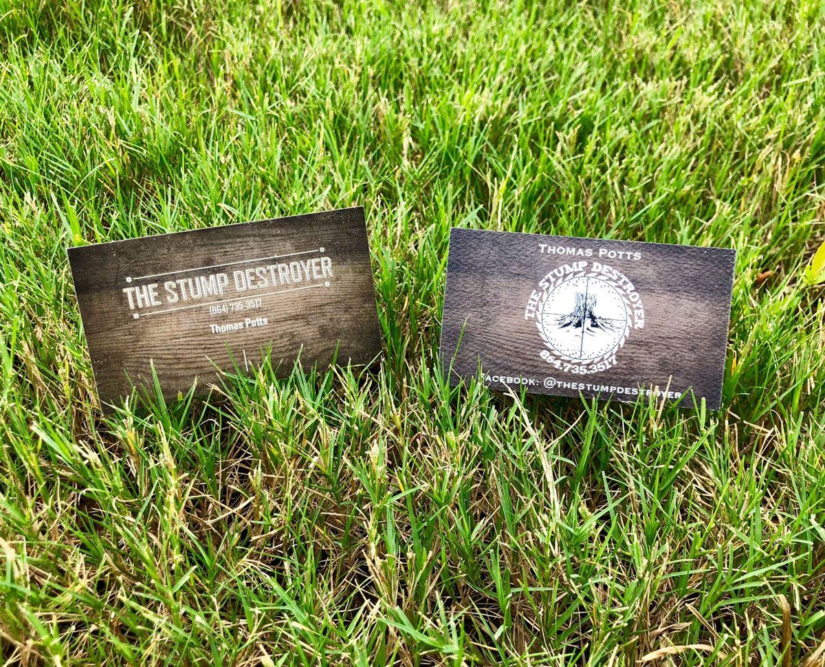 Two business cards are sitting on top of a lush green field.