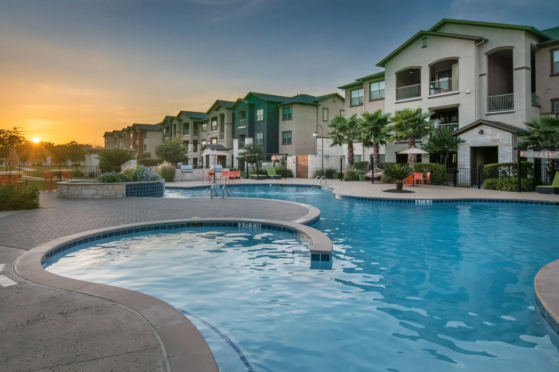 Sunset over a resort-style pool at a multifamily community with lounge chairs and palm trees.