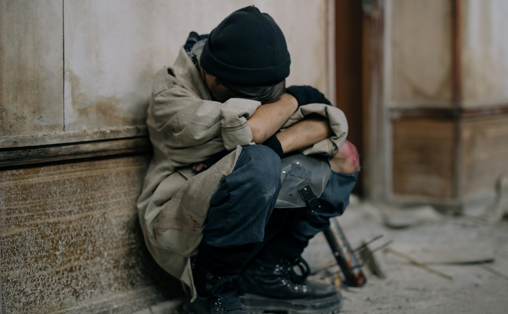 Man sits in despair on concrete steps, head in hands wearing dark beanie and jacket, illustrating men's mental health struggles, male depression, emotional breakdown, and the hidden psychological challenges men face beyond surface appearances.