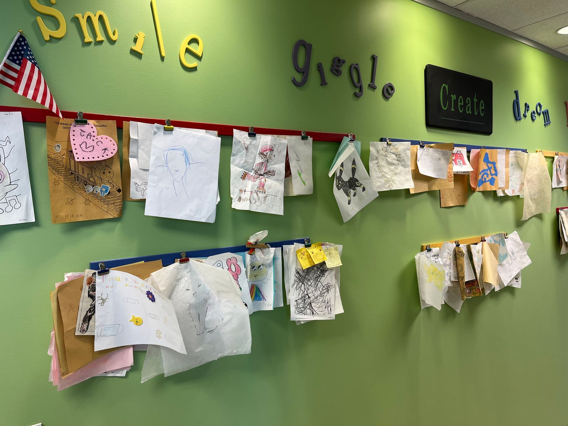 Green wall with children's artwork clipped to red/blue lines. 