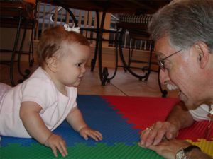 Man and baby girl looking at each other on a colorful floor mat.
