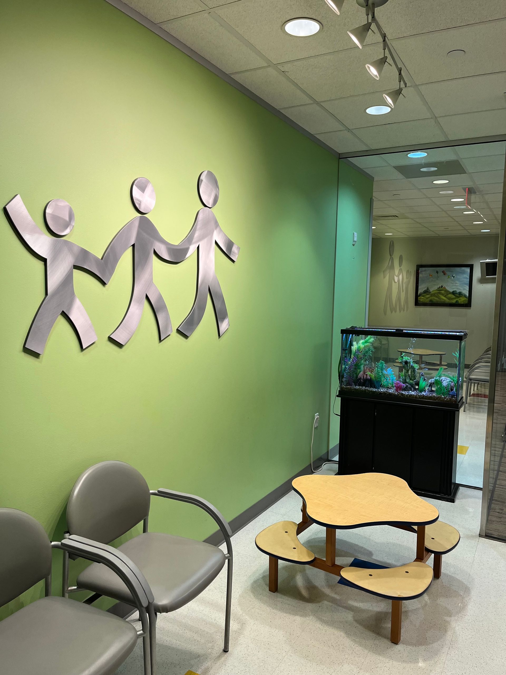 Waiting room with green wall, chairs, kids table, and aquarium.