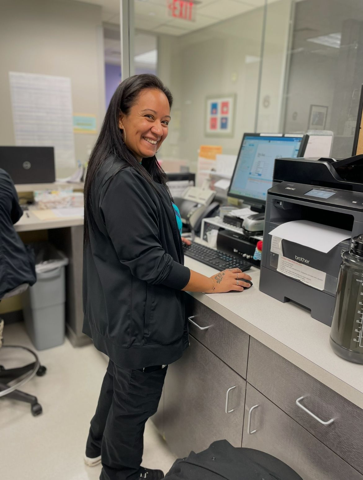 Smiling woman in an office, sitting in front of a computer.