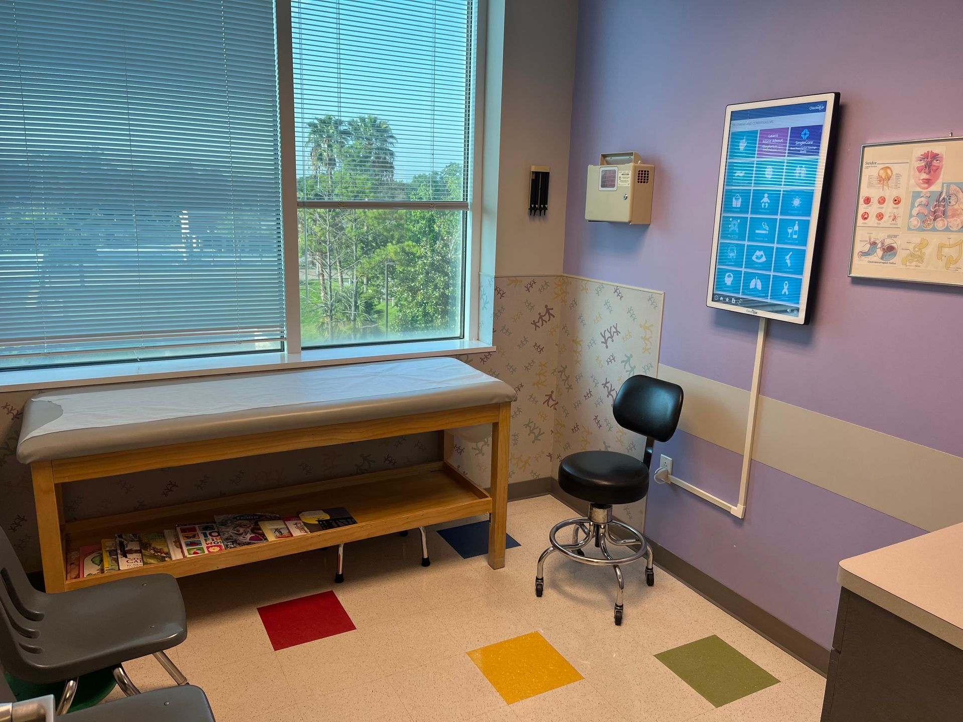 Exam room with examination table, stool, and medical charts on a purple wall.