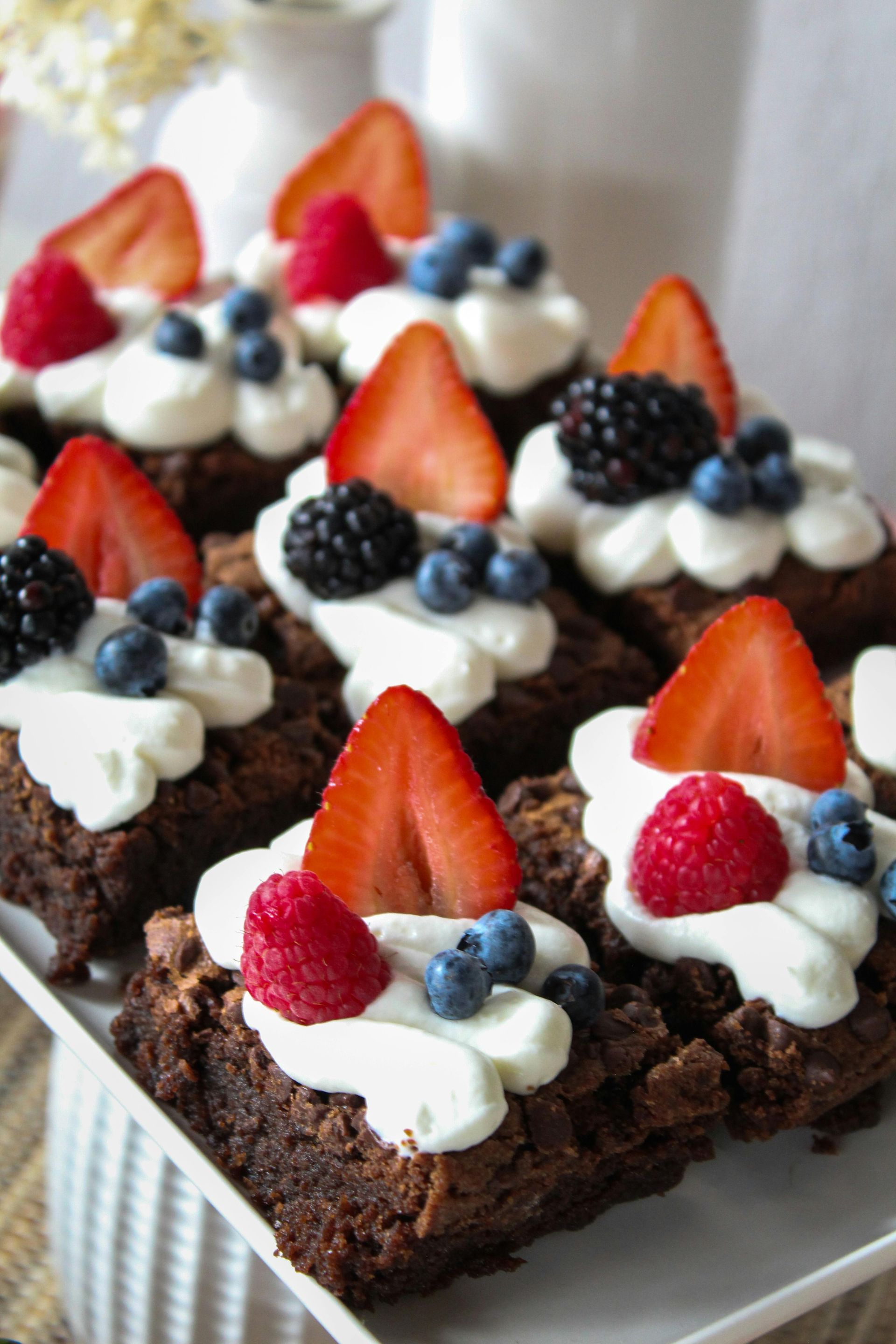 Brownie squares topped with whipped cream, berries (strawberries, blueberries, raspberries, blackberries).