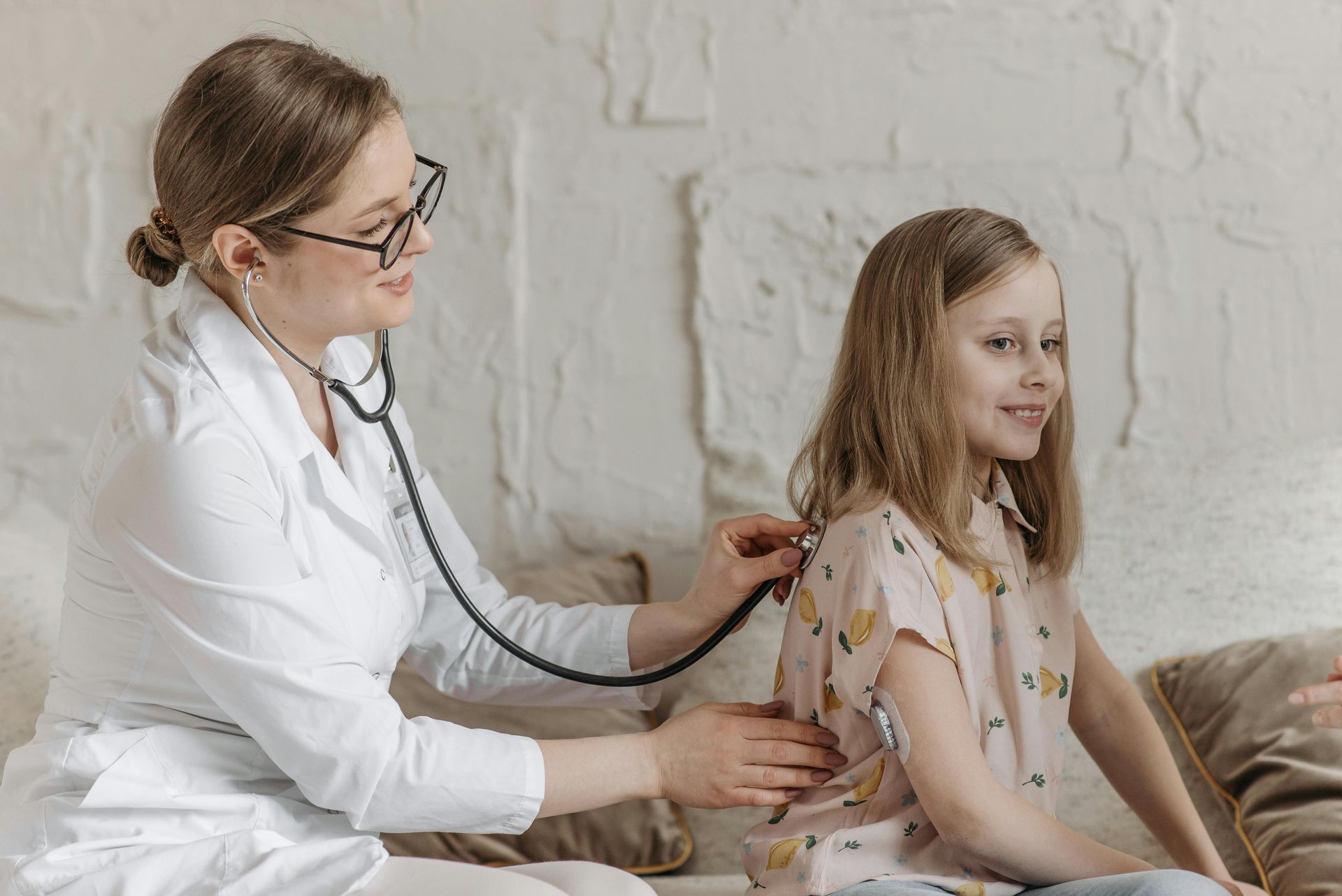 Female doctor with a stethoscope checking the back of a young girl.
