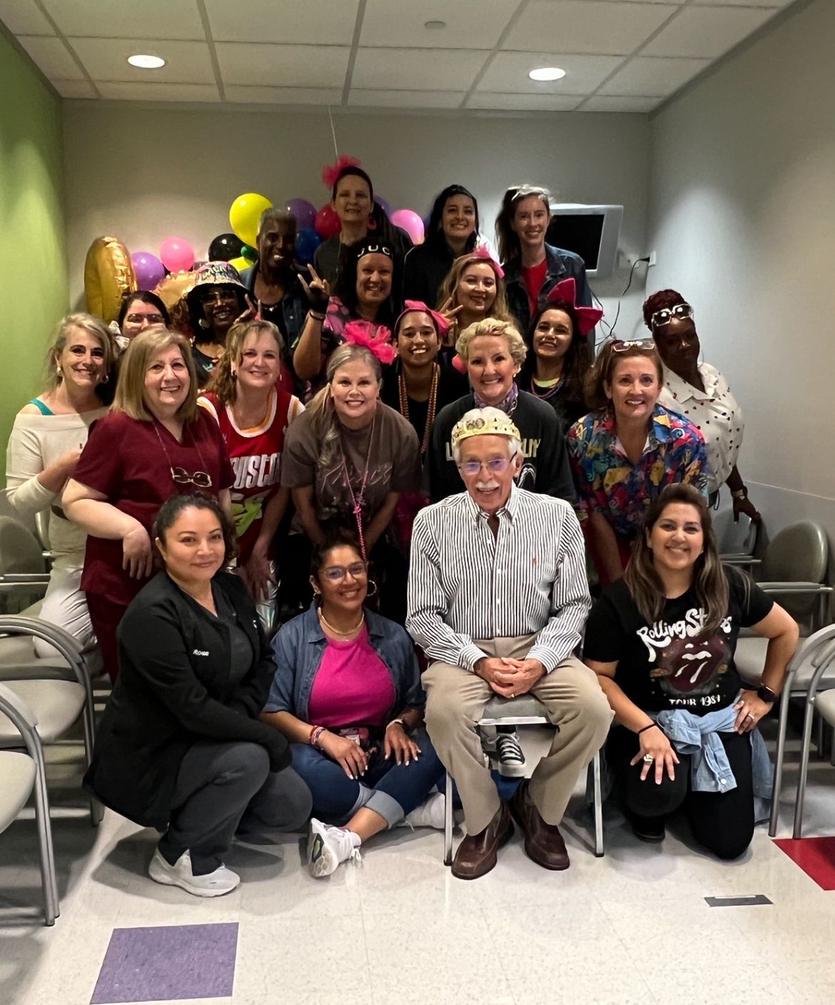 Group of people gathered indoors, smiling. Several women wear bows, and a man sits in the center.