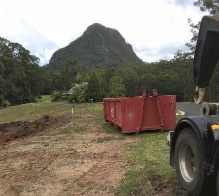 A Red Dumpster with The Lid Open Is Sitting In Front of Mountain — Chilli Bins Skip Bins in Glenview, QLD