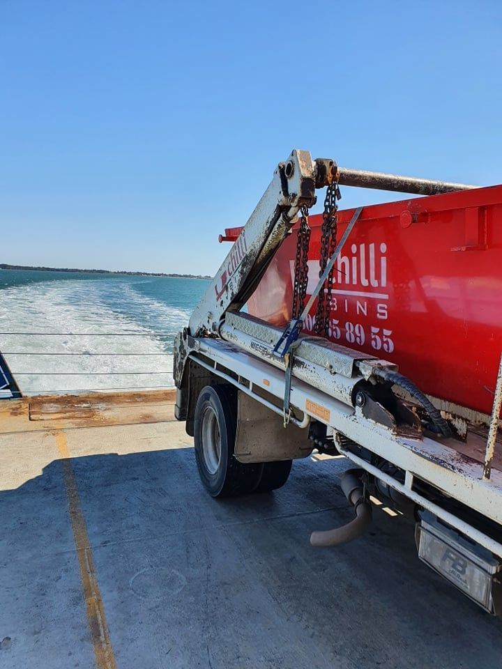 Red Bin Truck on a Ferry, Heading Towards Water With White Wake — Chilli Bins Skip Bins in Glenview, QLD