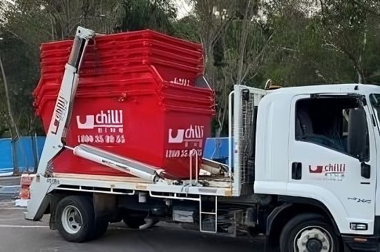 A Dump Truck with A Red Bin on The Back Is Parked in A Parking Lot — Chilli Bins Skip Bins in Caloundra, QLD