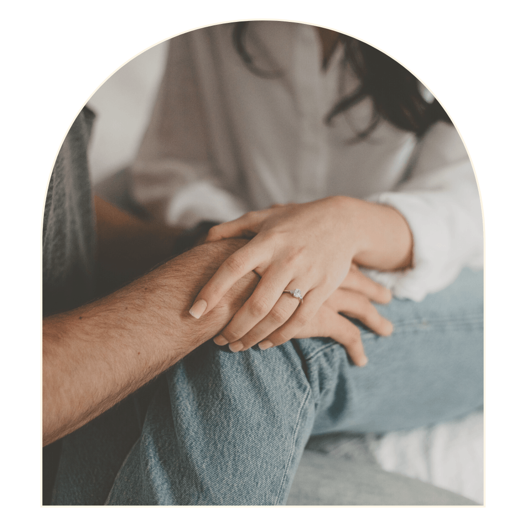 Couple holding hands, woman wearing engagement ring, sitting in denim jeans.