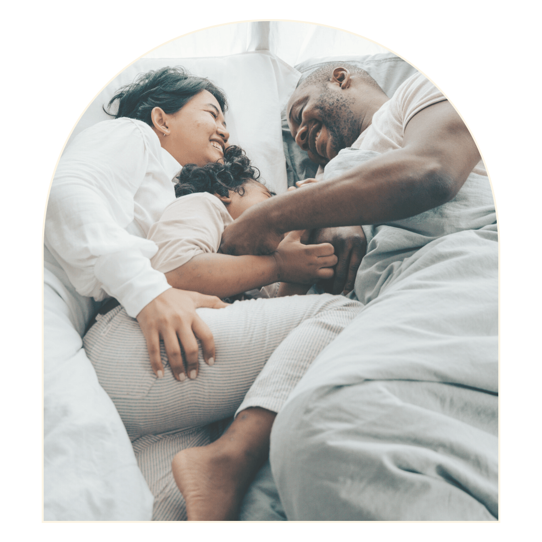 Family in bed, cuddling, laughing, and embracing each other under a white duvet.