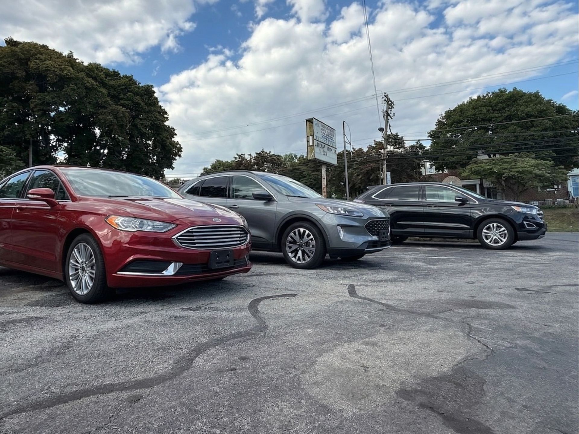 Three cars parked at White Auto Rental under a cloudy sky: a red sedan, a grey SUV, and a black sedan.