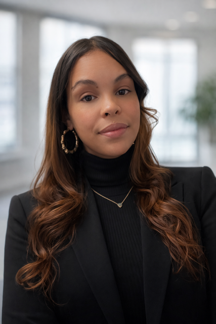 Woman wearing a black blazer and turtleneck, gold hoop earrings and necklace, looking at the camera.
