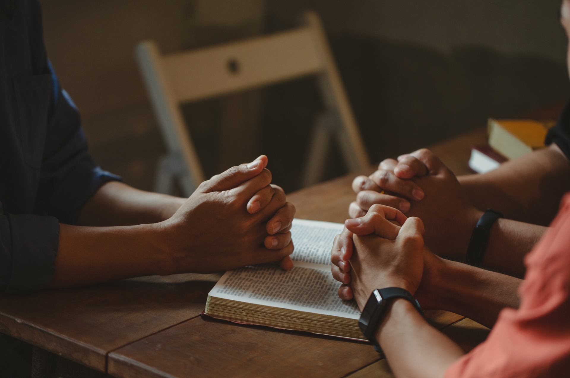 A group of people are sitting at a table with their hands folded in prayer.